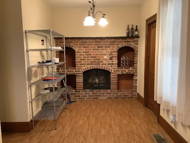 living room with visible vents, a brick fireplace, baseboards, a chandelier, and wood finished floors