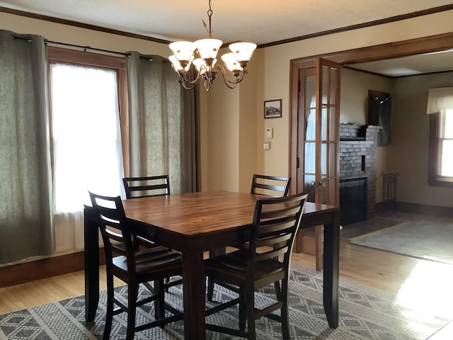 dining area featuring light wood-style floors, a brick fireplace, crown molding, and an inviting chandelier