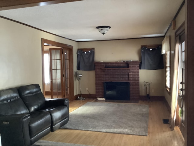 living area featuring visible vents, hardwood / wood-style flooring, crown molding, baseboards, and a brick fireplace