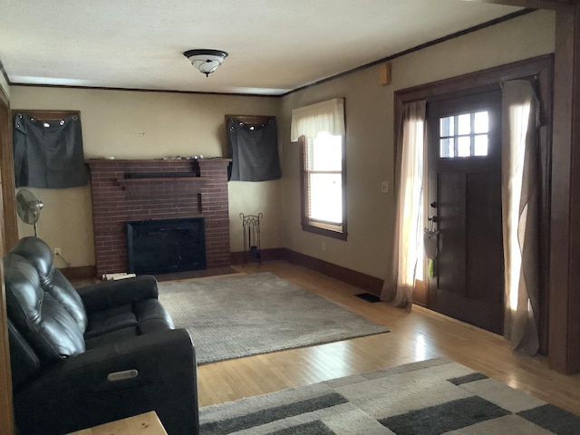 living room with a brick fireplace, crown molding, baseboards, and wood finished floors