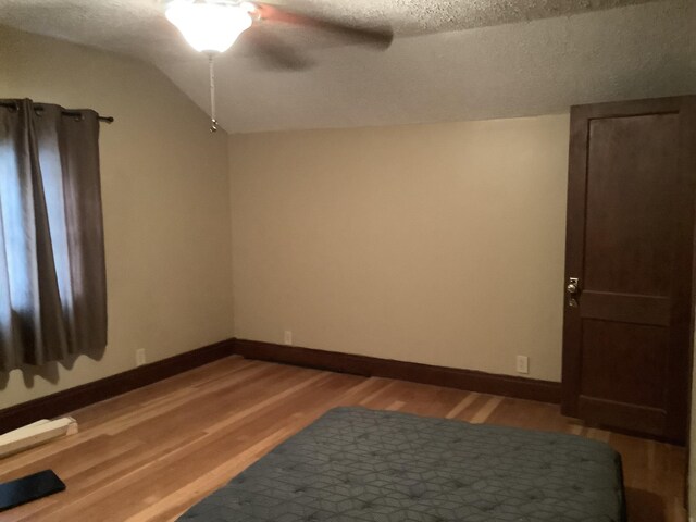 spare room featuring baseboards, light wood finished floors, a textured ceiling, and vaulted ceiling