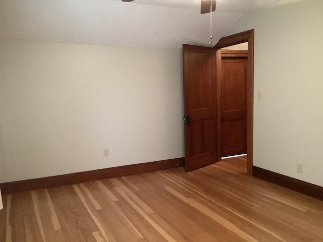 empty room with baseboards, light wood-style floors, and vaulted ceiling