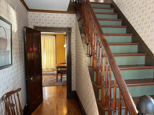 stairway featuring hardwood / wood-style flooring, ornamental molding, and a baseboard heating unit