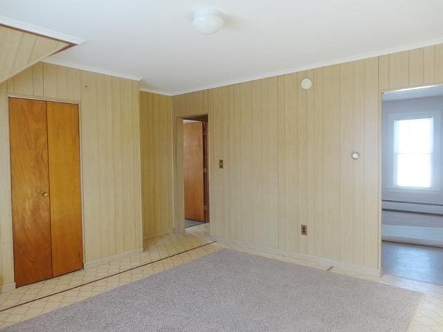 empty room with crown molding, a baseboard radiator, and wooden walls