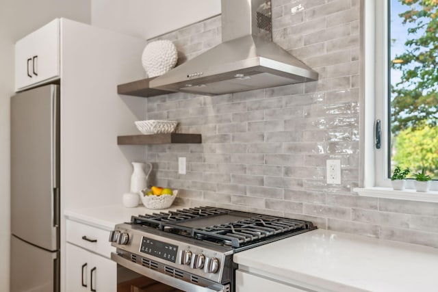 kitchen with stainless steel appliances, wall chimney range hood, white cabinets, and backsplash