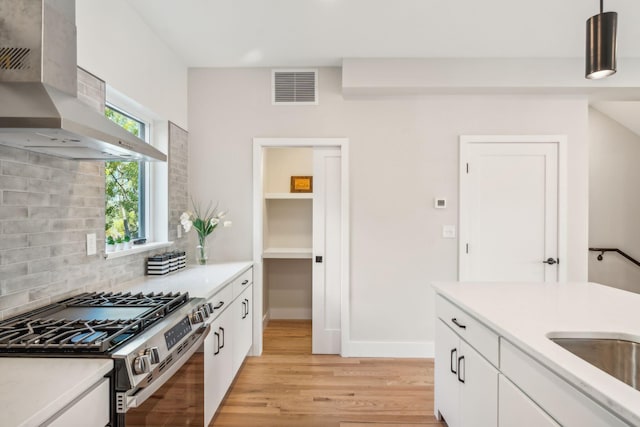 kitchen featuring extractor fan, stainless steel gas stove, tasteful backsplash, decorative light fixtures, and white cabinets