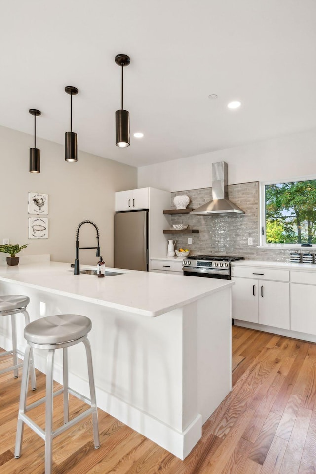 kitchen featuring pendant lighting, wall chimney range hood, sink, white cabinetry, and stainless steel appliances