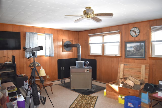 exercise room with a baseboard radiator, a wood stove, wooden walls, and ceiling fan