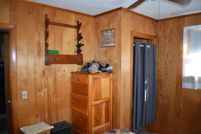 interior space with ceiling fan, ornamental molding, and wooden walls