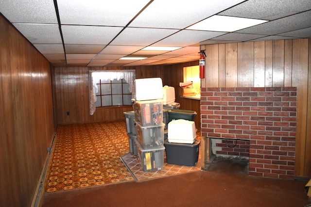 basement with a drop ceiling, baseboard heating, and wood walls