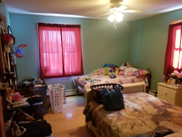 bedroom featuring a baseboard radiator, multiple windows, hardwood / wood-style flooring, and ceiling fan