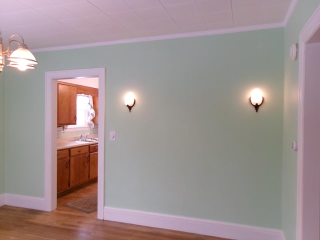 hall with ornamental molding, sink, an inviting chandelier, and light hardwood / wood-style flooring