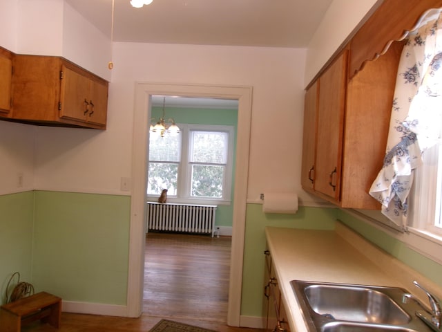 kitchen with sink, hanging light fixtures, radiator, a notable chandelier, and hardwood / wood-style floors