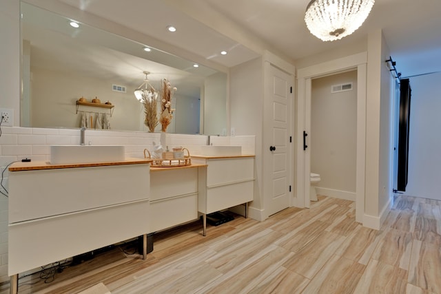 bathroom featuring tasteful backsplash, a notable chandelier, vanity, wood-type flooring, and toilet