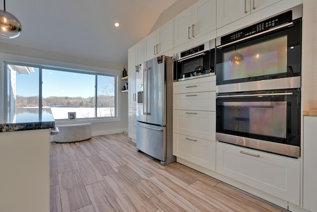 kitchen featuring white cabinetry, decorative light fixtures, vaulted ceiling, appliances with stainless steel finishes, and dark stone counters