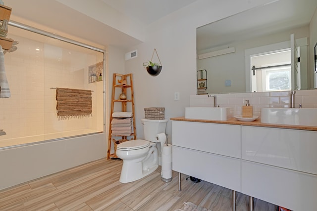 full bathroom featuring toilet, combined bath / shower with glass door, vanity, hardwood / wood-style flooring, and backsplash