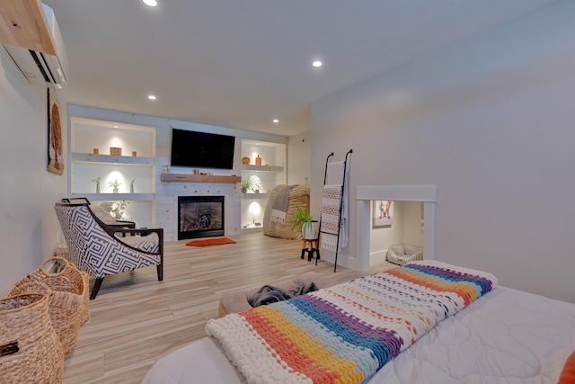 bedroom featuring a wall mounted air conditioner, light hardwood / wood-style floors, and a large fireplace