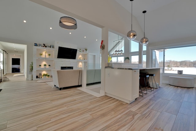 kitchen featuring a breakfast bar, a high ceiling, light hardwood / wood-style floors, a large fireplace, and decorative light fixtures