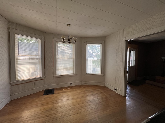 unfurnished dining area with hardwood / wood-style floors, plenty of natural light, and an inviting chandelier