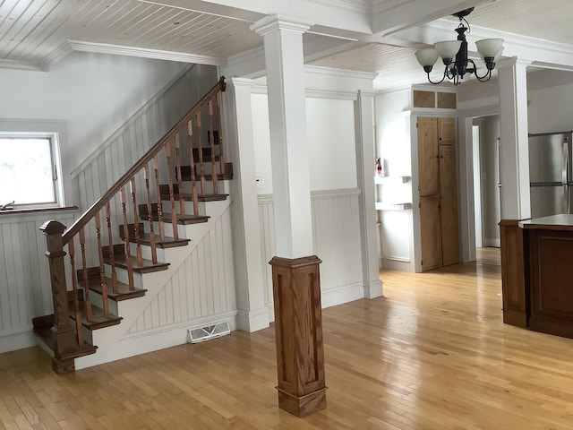 stairs with decorative columns, hardwood / wood-style flooring, a chandelier, beam ceiling, and ornamental molding
