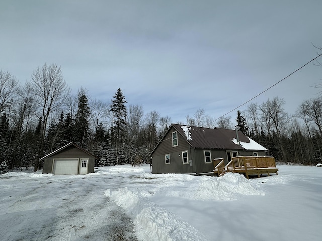 view of snowy exterior with a wooden deck, a garage, and an outdoor structure