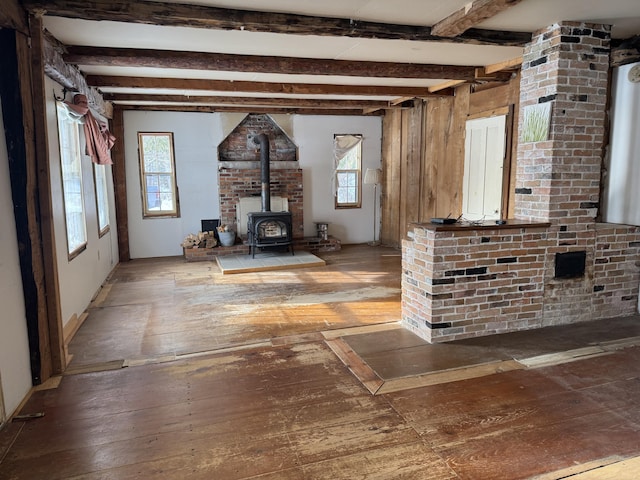 unfurnished living room featuring beamed ceiling, hardwood / wood-style flooring, and a wood stove