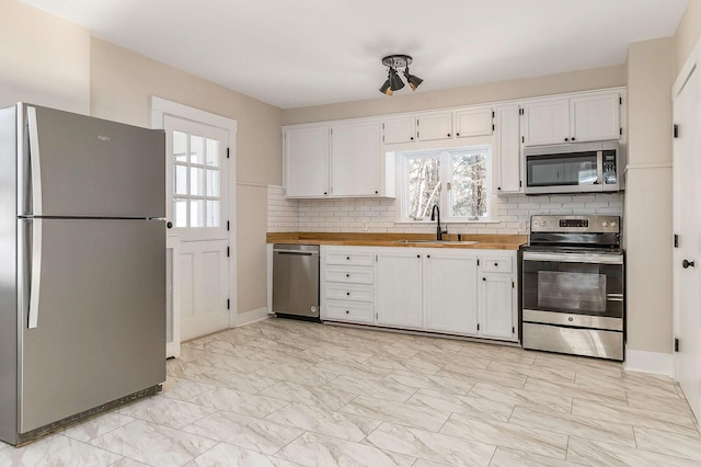 kitchen with appliances with stainless steel finishes, wood counters, sink, white cabinets, and decorative backsplash