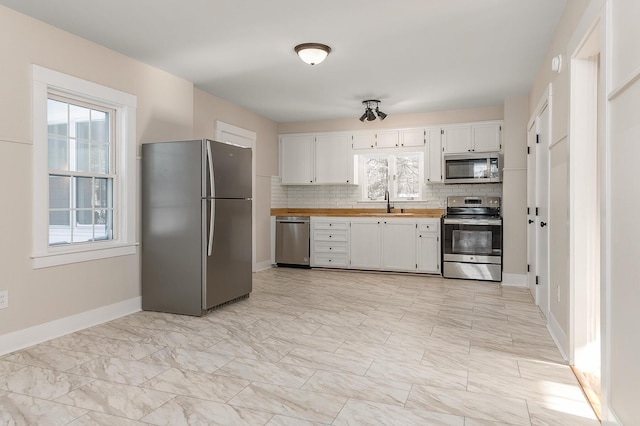 kitchen with appliances with stainless steel finishes, tasteful backsplash, white cabinetry, sink, and plenty of natural light