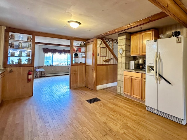 kitchen featuring a baseboard radiator, white refrigerator with ice dispenser, light hardwood / wood-style flooring, and wood walls