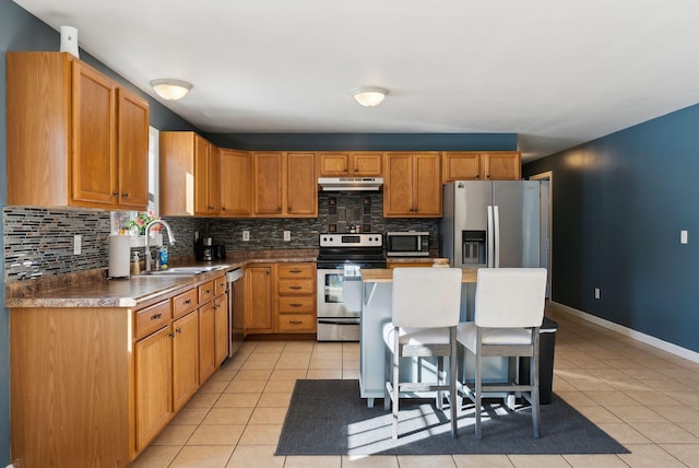 kitchen with sink, a breakfast bar area, light tile patterned floors, a kitchen island, and stainless steel appliances