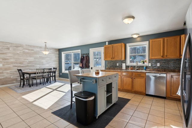 kitchen with light tile patterned flooring, stainless steel dishwasher, a kitchen island, pendant lighting, and decorative backsplash