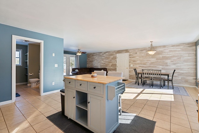 kitchen featuring a kitchen island, wood walls, decorative light fixtures, wooden counters, and light tile patterned floors