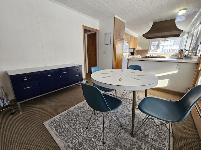 dining space with wooden walls and dark colored carpet