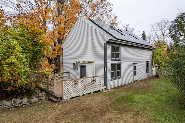 view of side of property with a wooden deck, a yard, and solar panels