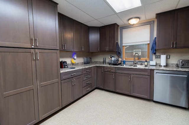 kitchen featuring dark brown cabinetry, sink, light stone counters, stainless steel dishwasher, and a drop ceiling