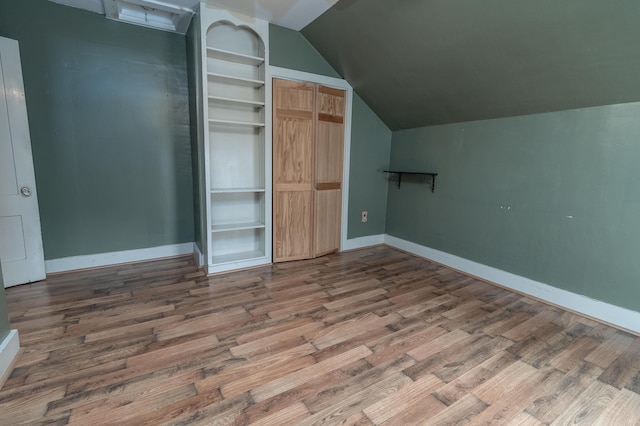 interior space featuring built in shelves, wood-type flooring, and vaulted ceiling