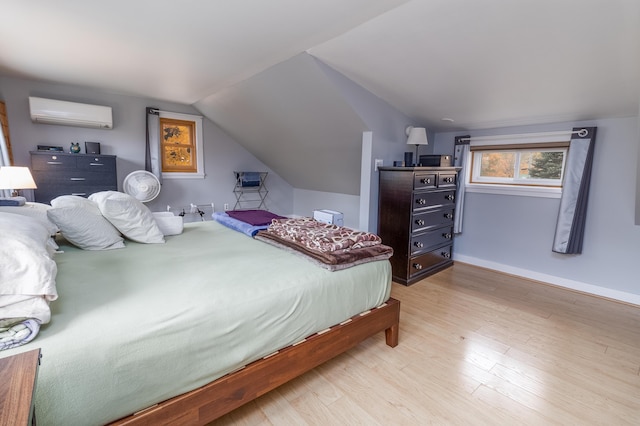 bedroom with lofted ceiling, a wall unit AC, and light wood-type flooring