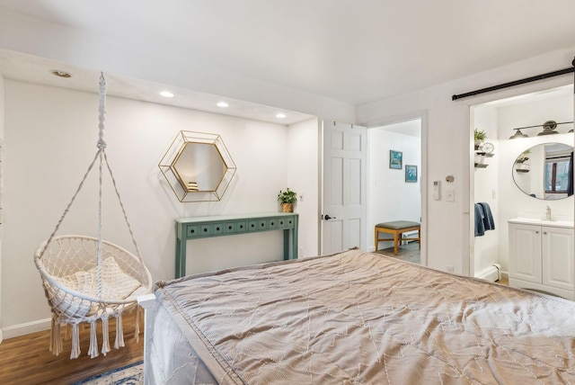 bedroom with ensuite bathroom, a barn door, and hardwood / wood-style floors