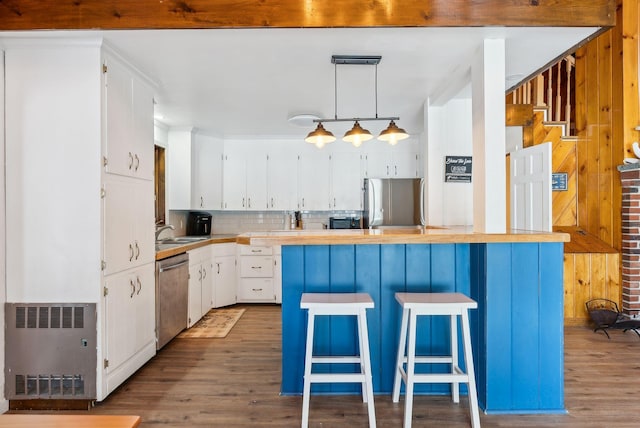 kitchen with appliances with stainless steel finishes, radiator, white cabinets, a kitchen breakfast bar, and hanging light fixtures