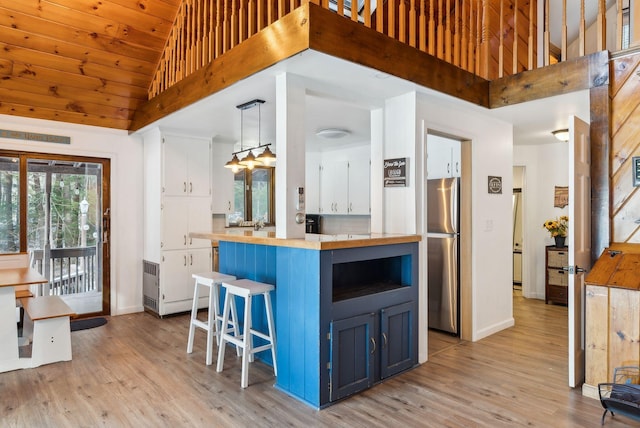 kitchen with a breakfast bar, decorative light fixtures, blue cabinets, white cabinetry, and stainless steel fridge