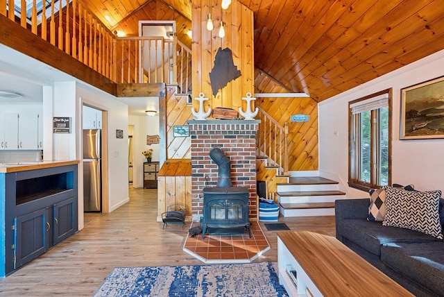 living room featuring high vaulted ceiling, wooden walls, a wood stove, light hardwood / wood-style floors, and wooden ceiling