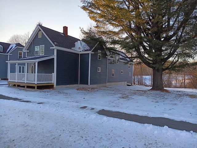 snow covered rear of property featuring covered porch