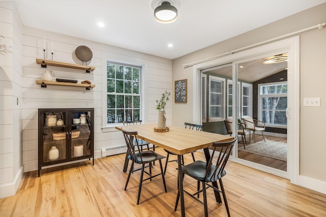 dining space featuring light wood-type flooring, wooden walls, a baseboard radiator, and lofted ceiling