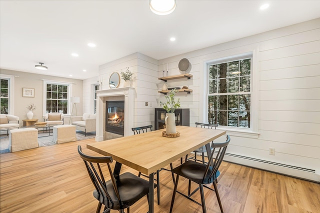 dining room with light hardwood / wood-style floors, wooden walls, and a baseboard radiator