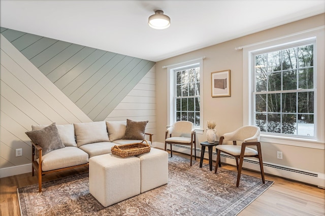 living area featuring hardwood / wood-style flooring, plenty of natural light, wooden walls, and a baseboard heating unit