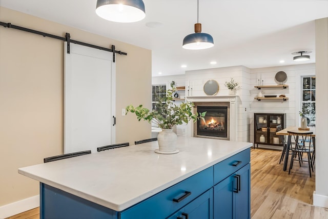 kitchen with blue cabinets, hanging light fixtures, a barn door, and light hardwood / wood-style floors