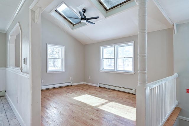 additional living space with vaulted ceiling with skylight, a baseboard radiator, light hardwood / wood-style floors, and ceiling fan