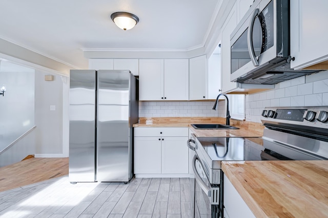 kitchen with wood counters, sink, white cabinetry, crown molding, and appliances with stainless steel finishes