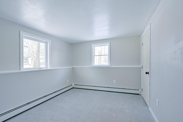 empty room featuring baseboard heating, plenty of natural light, light carpet, and a textured ceiling