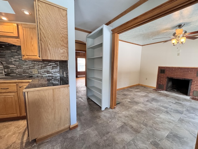 kitchen with a fireplace, a sink, tasteful backsplash, dark countertops, and crown molding